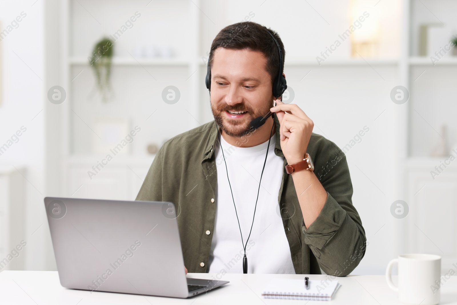 Photo of Interpreter in headset having video chat via laptop at white table indoors