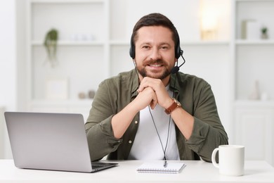 Photo of Interpreter in headset having video chat via laptop at white table indoors