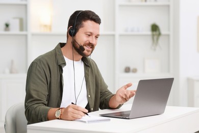 Interpreter in headset having video chat via laptop at white table indoors