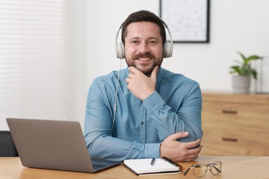 Interpreter in headphones having video chat via laptop at wooden table indoors