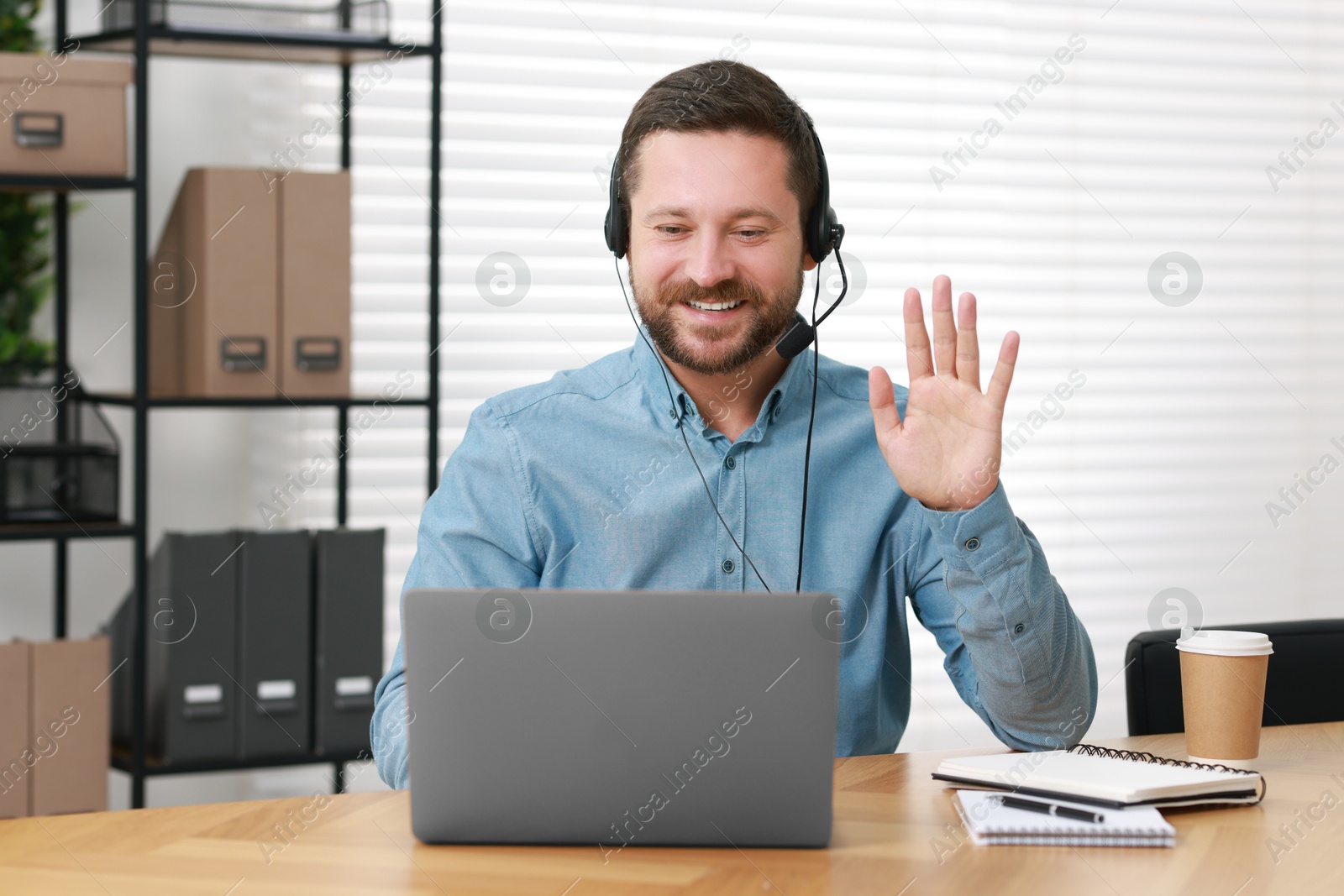 Photo of Interpreter in headset having video chat via laptop at wooden table indoors