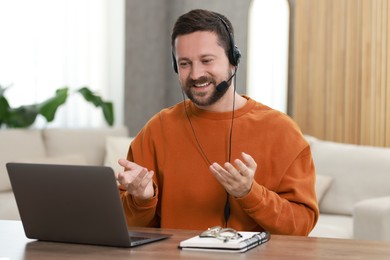 Photo of Interpreter in headset having video chat via laptop at wooden table indoors