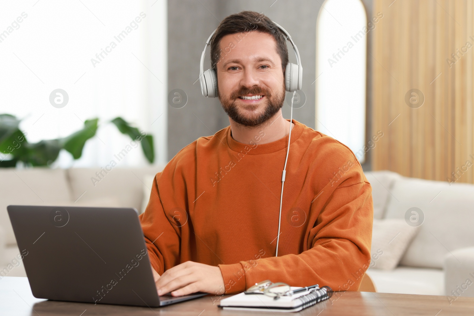 Photo of Interpreter in headphones having video chat via laptop at wooden table indoors