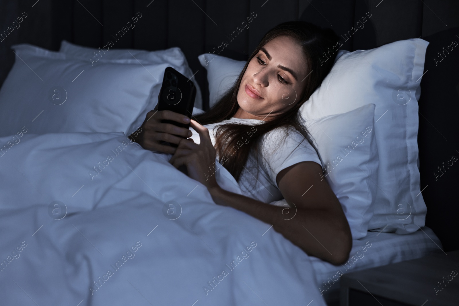 Photo of Bad habit. Young woman using smartphone in bed at night