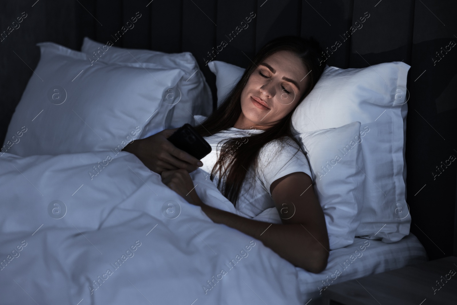 Photo of Bad habit. Young woman using smartphone in bed at night