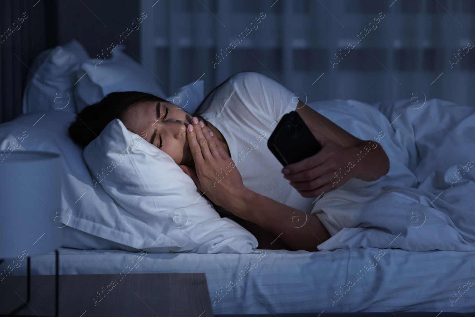 Photo of Bad habit. Young woman using smartphone in bed at night