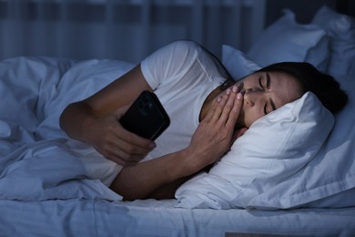 Photo of Bad habit. Young woman using smartphone in bed at night