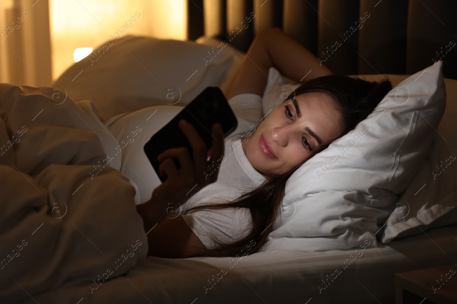 Photo of Bad habit. Young woman using smartphone in bed at night