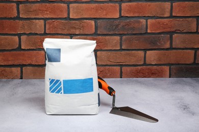 Photo of Bag of cement and trowel on light textured table against red brick wall. Space for text