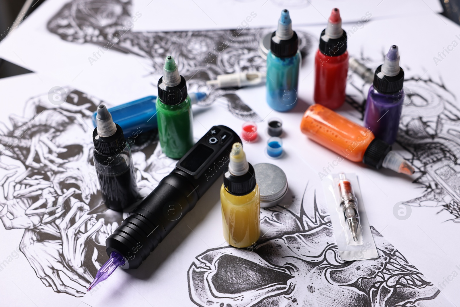 Photo of Tattoo machine and colorful inks on different sketches