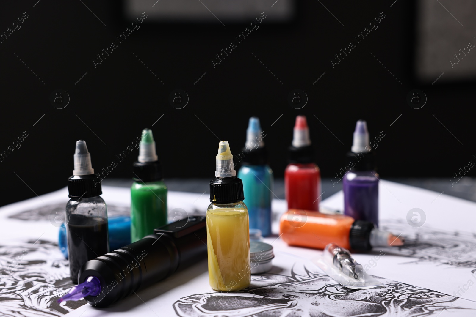 Photo of Tattoo machine, colorful inks and different sketches in salon