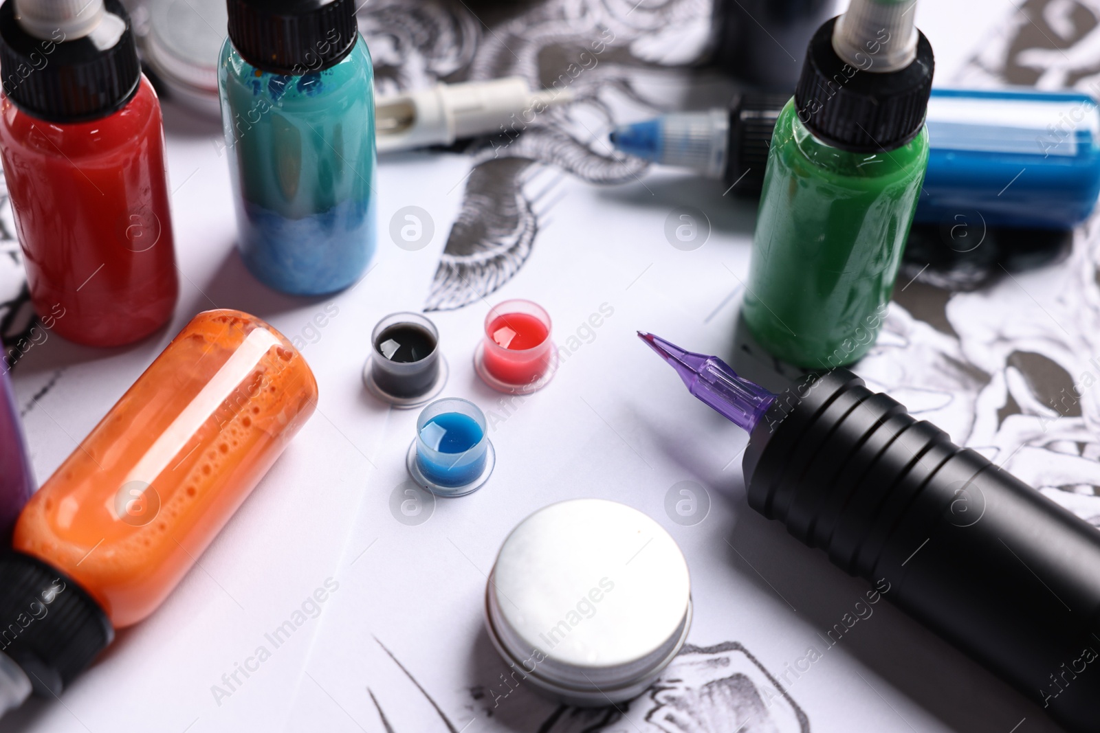 Photo of Tattoo machine and colorful inks on different sketches, closeup