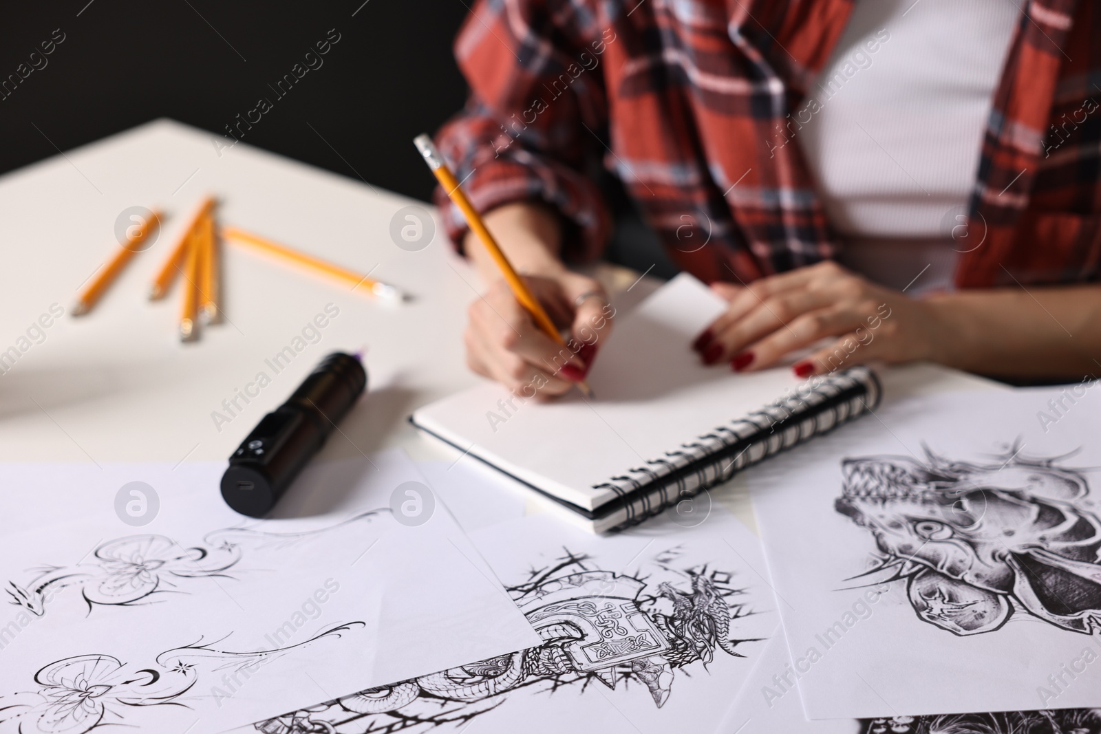 Photo of Tattoo artist drawing sketch with pencil at white table, closeup