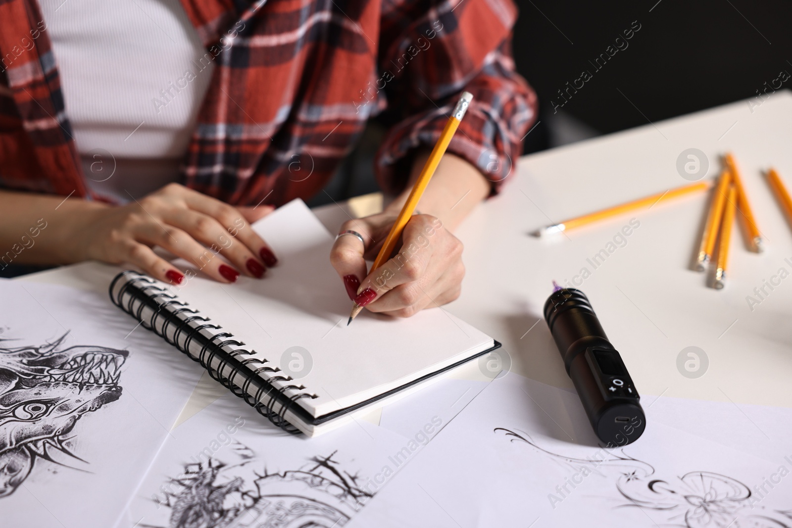 Photo of Tattoo artist drawing sketch with pencil at white table, closeup