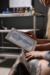 Photo of Tattoo artist showing tablet with sketch to client in salon, closeup