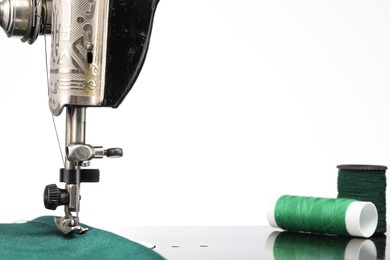 Photo of Sewing machine with green fabric and spools of threads isolated on white