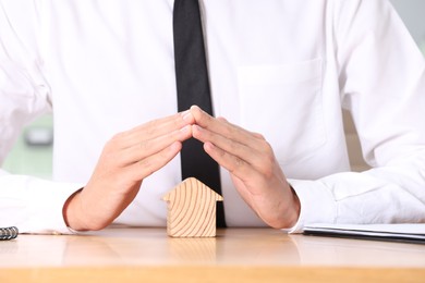 Photo of Property insurance. Real estate agent protecting house figure at table, closeup