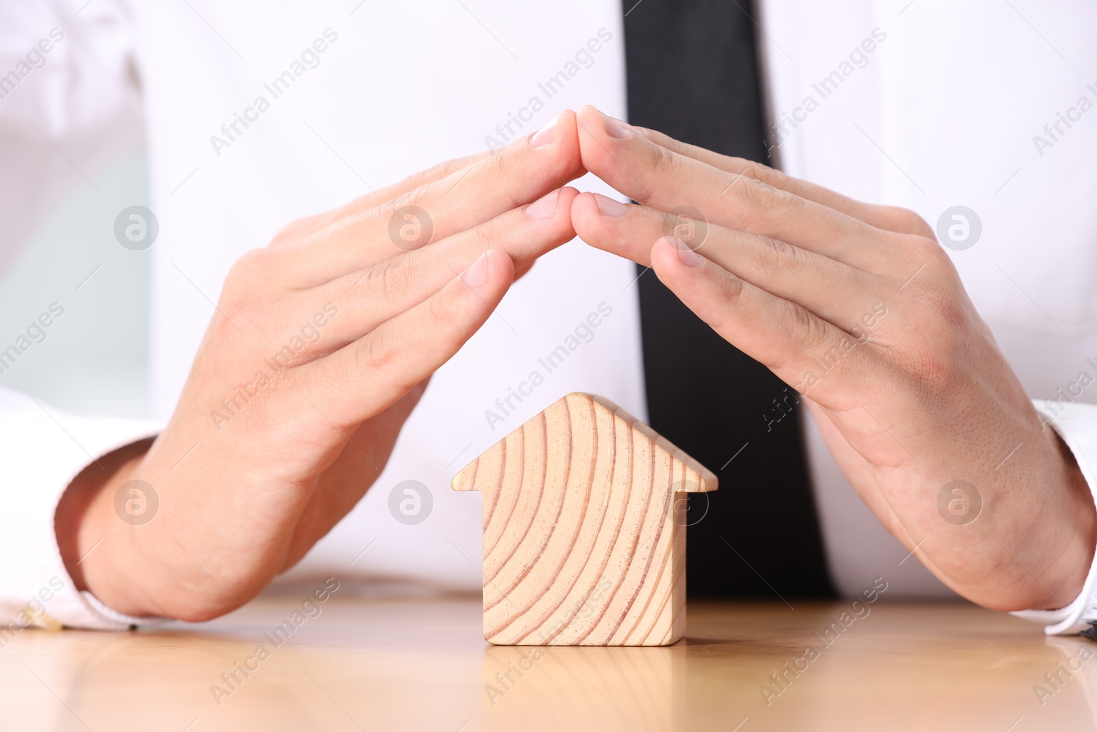 Photo of Property insurance. Real estate agent protecting house figure at table, closeup