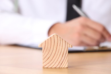 Photo of Property insurance. Real estate agent working at table indoors, focus on wooden house figure