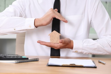 Photo of Property insurance. Real estate agent protecting house figure at table, closeup