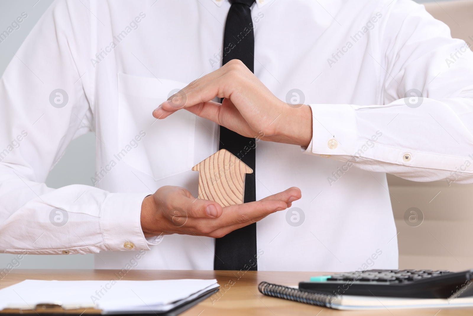 Photo of Property insurance. Real estate agent protecting house figure at table, closeup