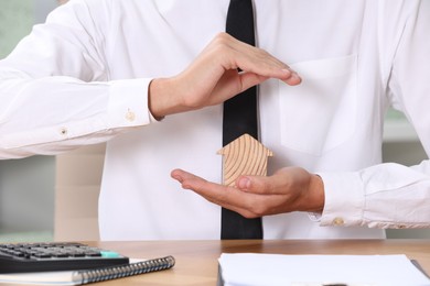 Photo of Property insurance. Real estate agent protecting house figure at table, closeup