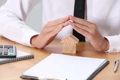 Photo of Property insurance. Real estate agent protecting house figure at wooden table, closeup