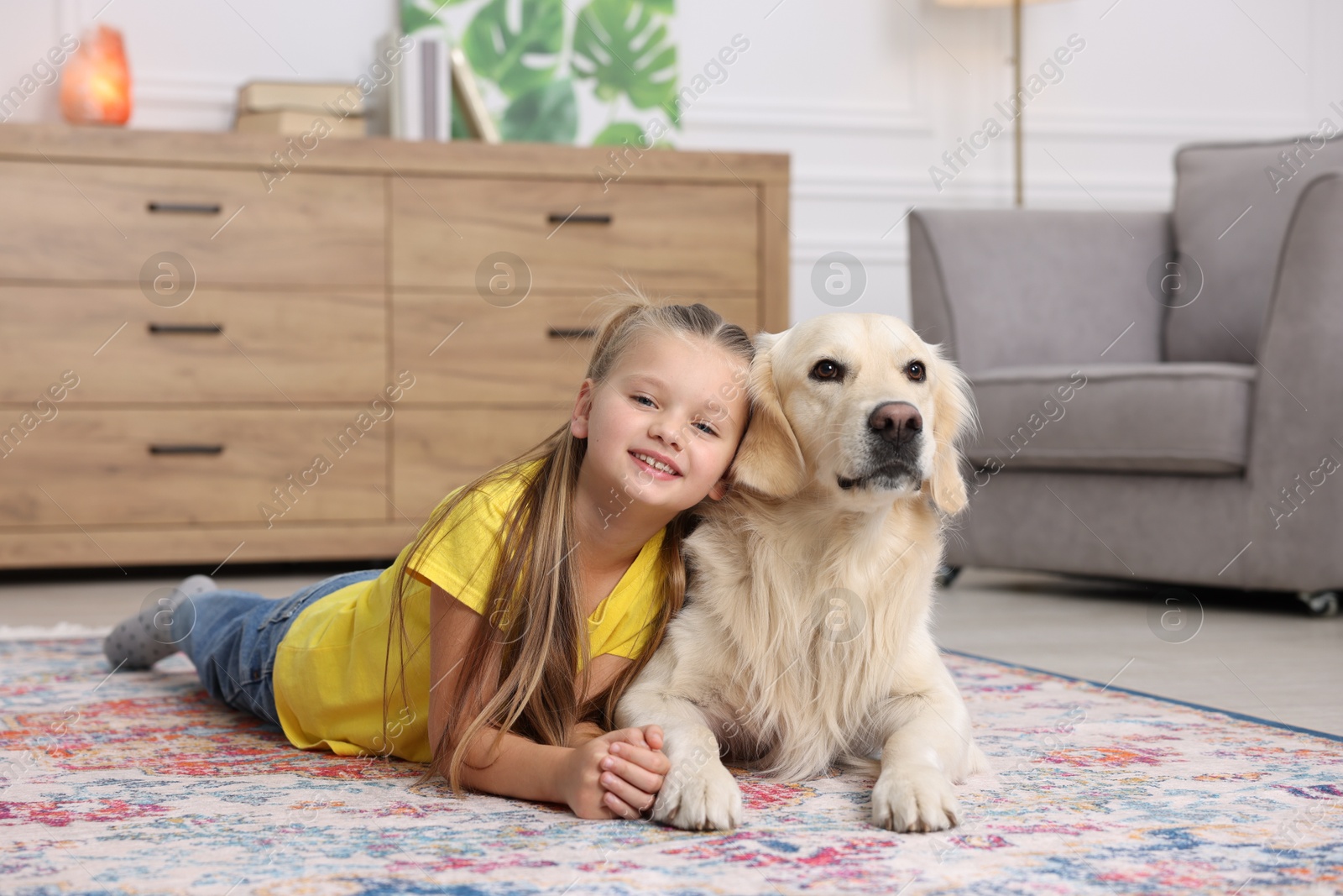 Photo of Girl with cute Golden Retriever dog lying on rug at home