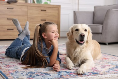 Girl with cute Golden Retriever dog lying on rug at home