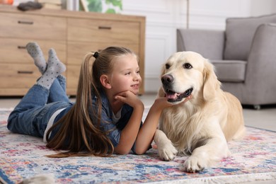 Photo of Girl with cute Golden Retriever dog lying on rug at home