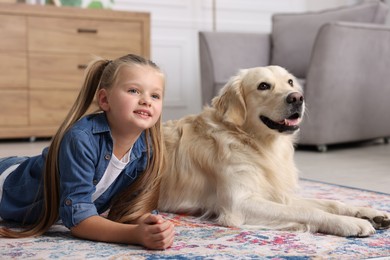 Girl with cute Golden Retriever dog lying on rug at home