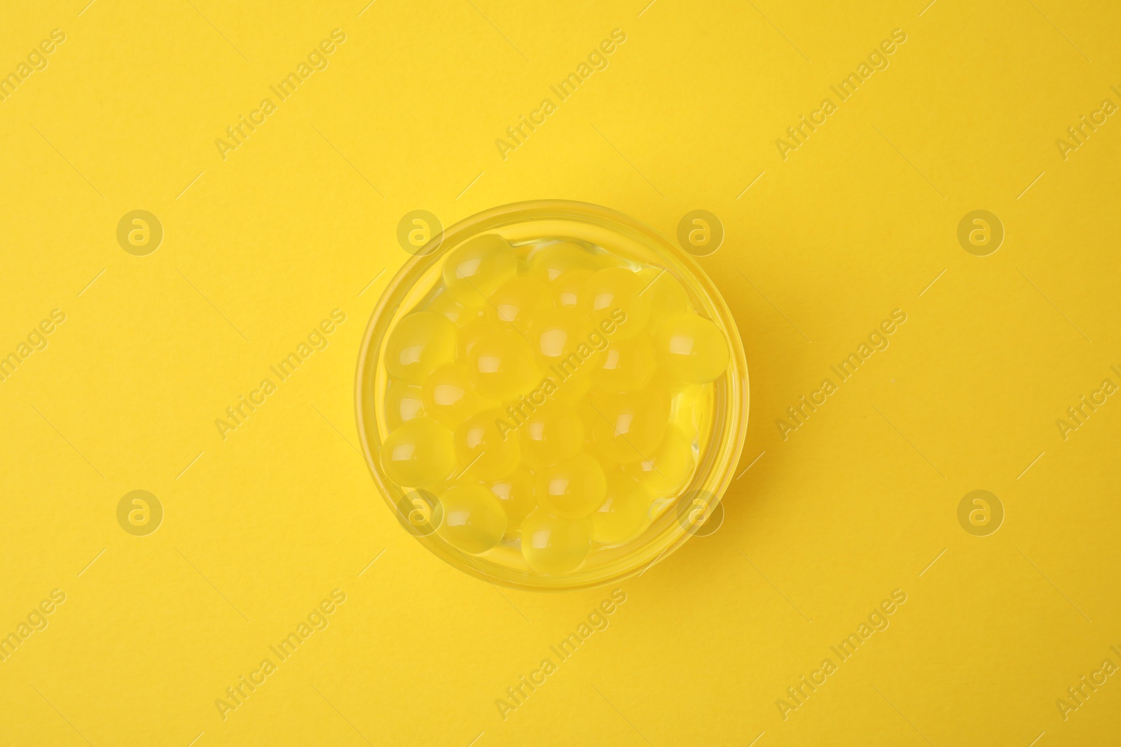 Photo of Bright tapioca pearls in bowl on yellow background, top view