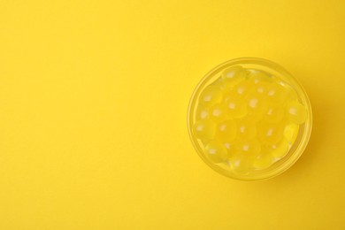 Photo of Bright tapioca pearls in bowl on yellow background, top view. Space for text