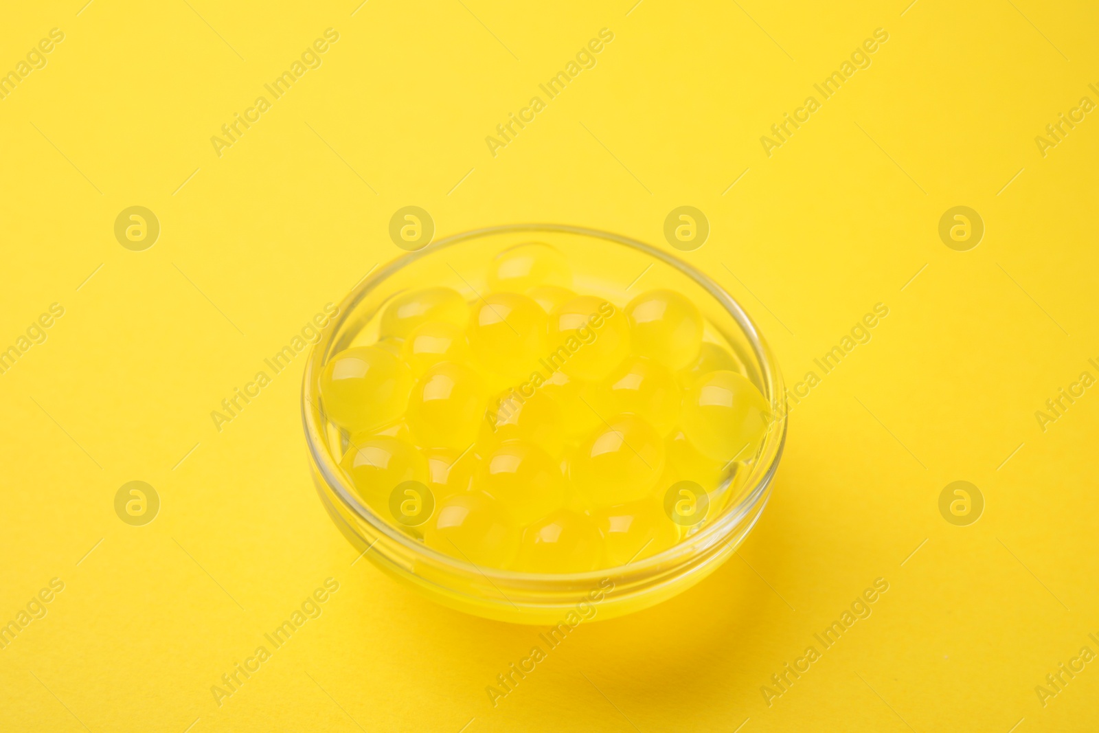 Photo of Bright tapioca pearls in bowl on yellow background, closeup