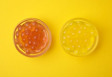 Photo of Bright tapioca pearls in bowls on yellow background, flat lay