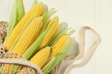 Photo of Many fresh ripe corncobs with green husks on white wooden table, top view