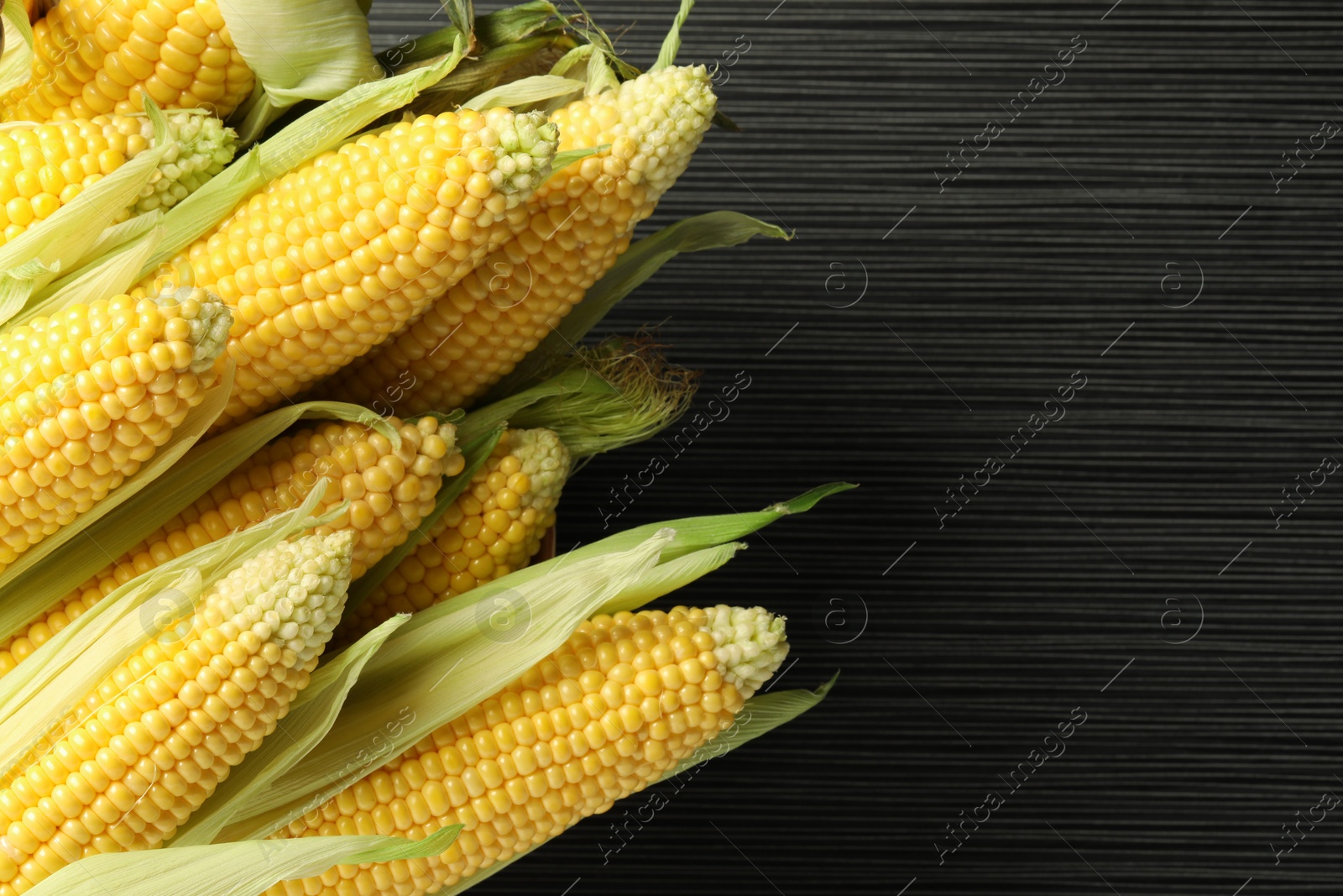 Photo of Many fresh ripe corncobs with green husks on wooden table, closeup. Space for text