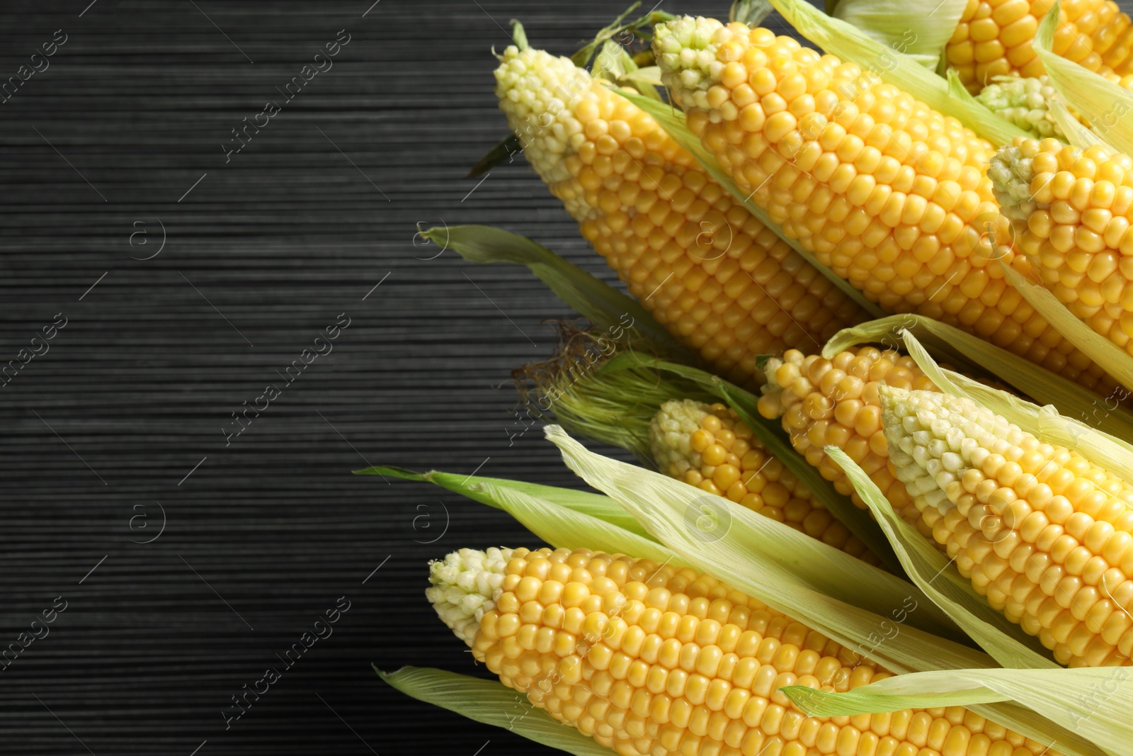 Photo of Many fresh ripe corncobs with green husks on wooden table, closeup. Space for text