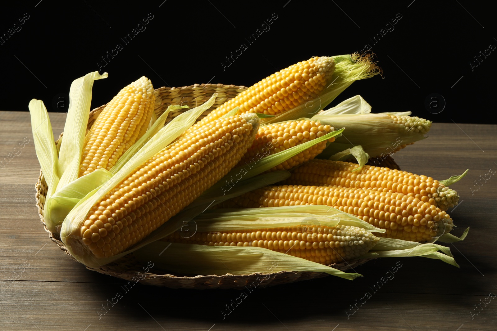 Photo of Many fresh ripe corncobs with green husks on wooden table