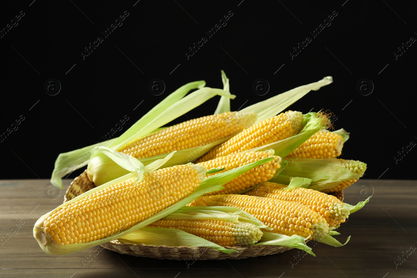 Photo of Many fresh ripe corncobs with green husks on wooden table