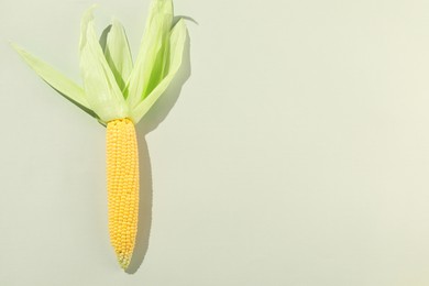 Photo of Fresh ripe corncob with green husks on light grey background, top view. Space for text