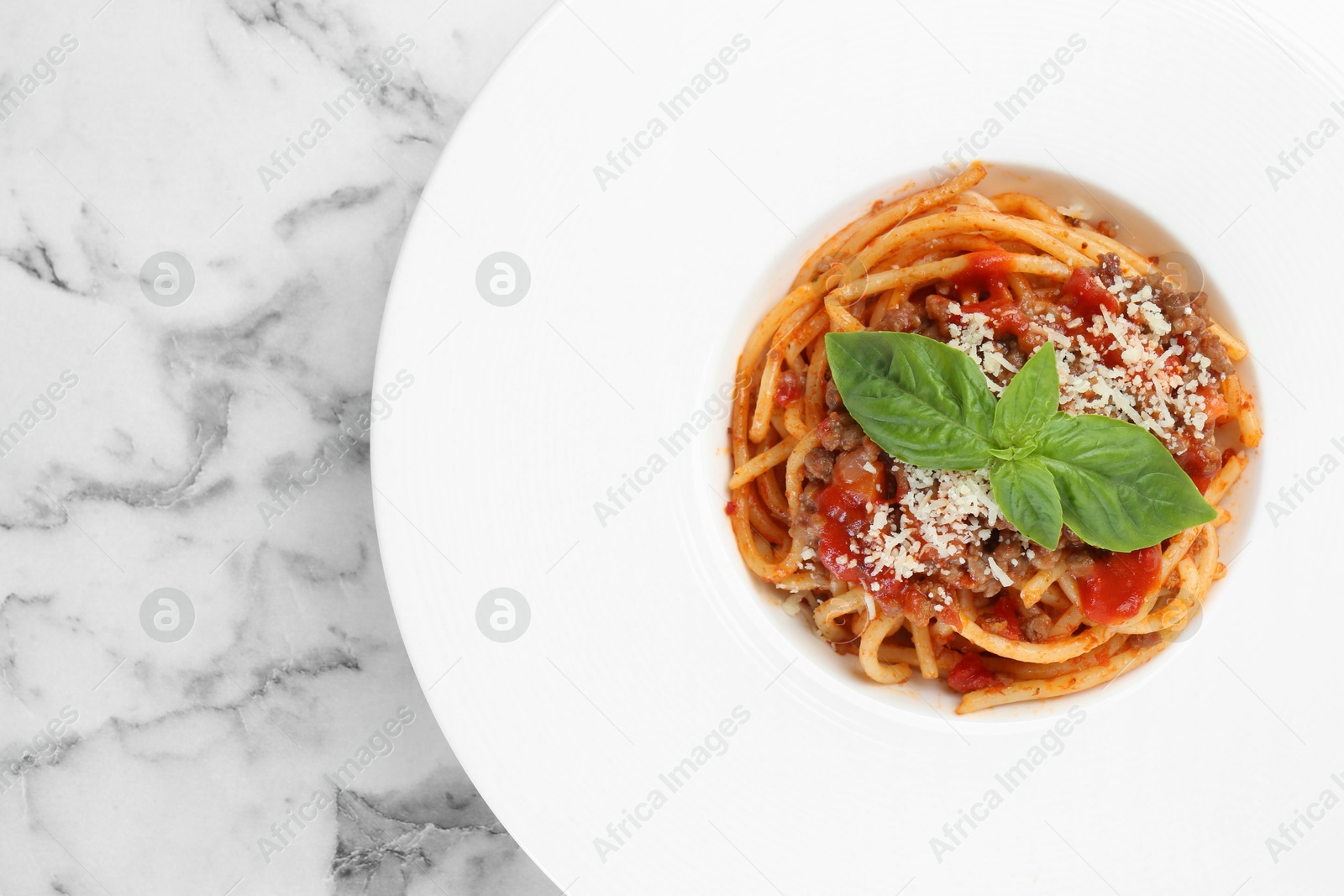 Photo of Delicious pasta bolognese with basil on white marble table, top view