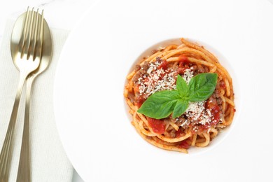 Photo of Delicious pasta bolognese with basil and cutlery on table, top view