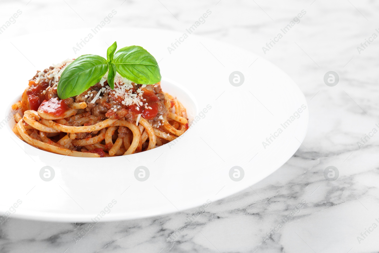 Photo of Delicious pasta bolognese with basil on white marble table, closeup