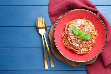 Photo of Delicious pasta bolognese with basil and cutlery on blue wooden table, top view. Space for text