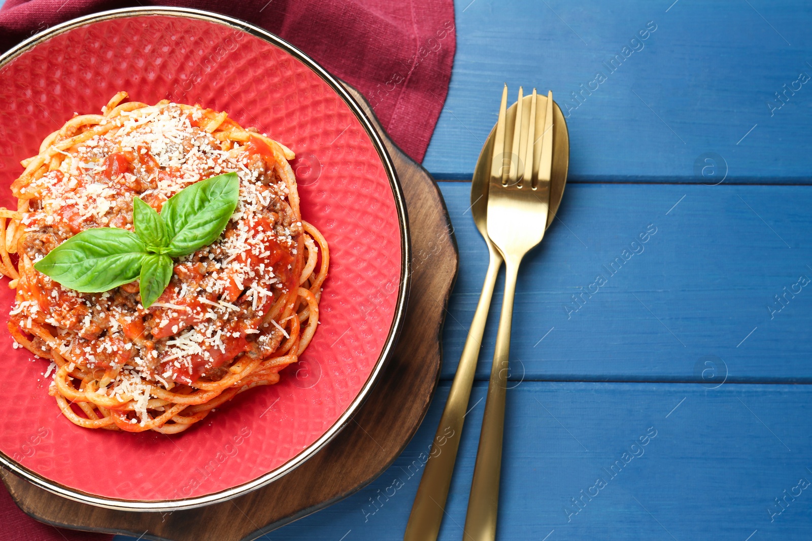 Photo of Delicious pasta bolognese with basil and cutlery on blue wooden table, top view. Space for text