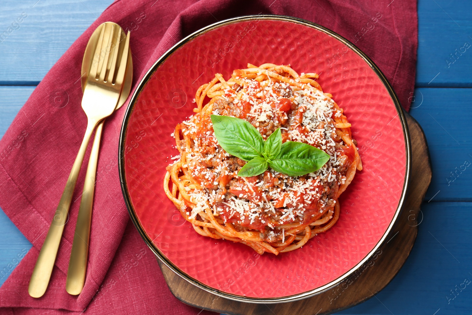 Photo of Delicious pasta bolognese with basil and cutlery on blue wooden table, top view