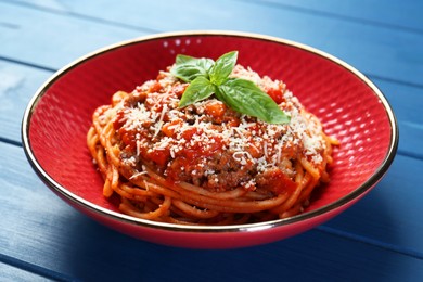 Photo of Delicious pasta bolognese with basil on blue wooden table, closeup