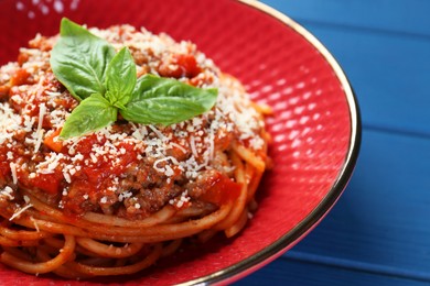 Photo of Delicious pasta bolognese with basil on blue wooden table, closeup