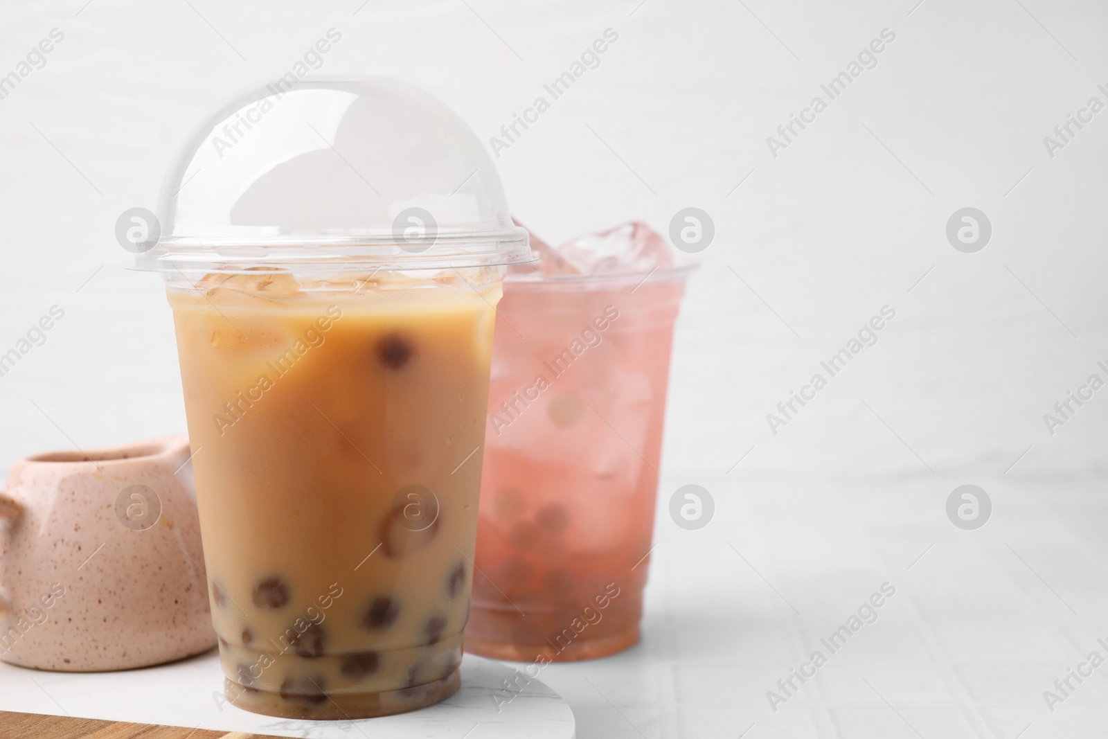 Photo of Tasty bubble tea in plastic cups on white tiled table, space for text